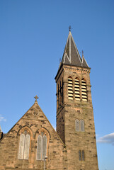Fototapeta premium Stone Church with Gable-Tower & Spire seen from below against blues Sky 