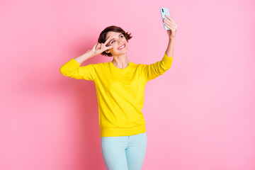 Obraz na płótnie Canvas Photo of young pretty sweet lovely smiling positive girl take selfie on phone show v-sign on eye isolated on pink color background