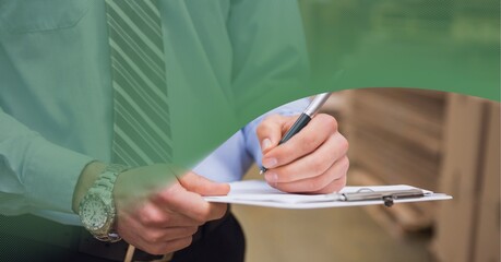 Green technology background over mid section of supervisor writing on clipboard at warehouse