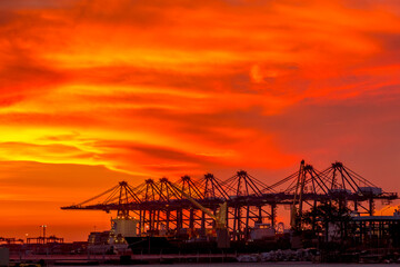 Fototapeta na wymiar Sky burst with silhouette Crane bridge during sunset at Container terminal seaport