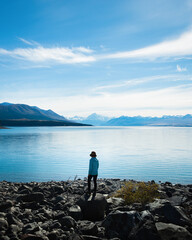 Woman standing on the shore of Lake Pukaki, enjoying the views of Mt Cook and Southern Alps, South Island. Vertical format.
