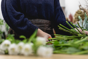 View of a young woman working as florist in a small shop and chopping flowers sprigs with a shear, business woman entrepreneur concept.