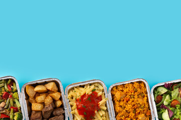 Take away healthy food in foil boxes on blue background. Copy space