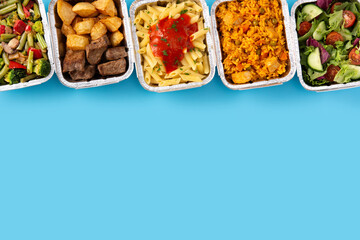 Take away healthy food in foil boxes on blue background. Copy space