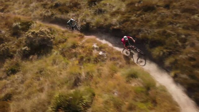 Two mountain bike riders following each other racing along dirt trail in the New Zealand alpine mountains.