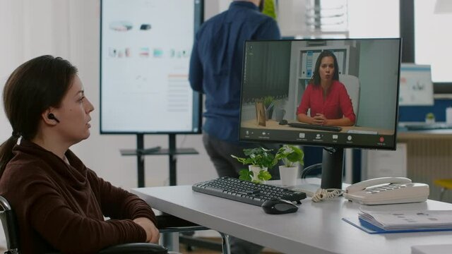 Invalid handicapped entrepreneur discussing during video conference using headset working in start up office at financial project sitting in wheelchair in workplace. Manager talking on virtual meeting