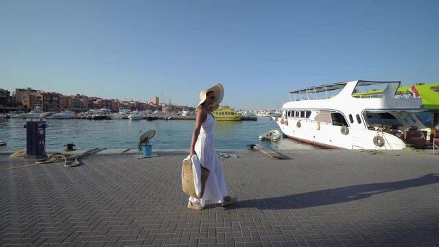 Attractive woman in white dress and straw hat on the pier in Hurghada, Egypt enjoying on her exotic vacation