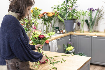 Rear view of a young woman working as florist and designing a new bouquet for wedding creation in her flower shop, young businesswoman concept.