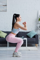 side view of brunette woman in sportswear exercising in awkward pose with clenched hands