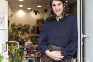 Portrait of a young cheerful woman working as florist standing at her own business shop entrance. Businesswoman concept. - obrazy, fototapety, plakaty