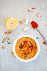 Flat lay of a bowl of delicious hummus with olive oil, garlic and paprika on a grey background.