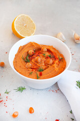 A bowl of delicious hummus with olive oil, garlic and paprika on a grey background.