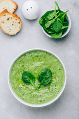 Green creamy spinach soup with baguette toasts on a gray concrete background.