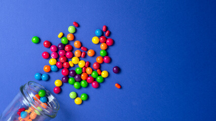 colorful candies poured from a glass jar on a colored background