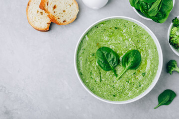 Green creamy spinach and broccoli soup with baguette toasts on a gray concrete background.