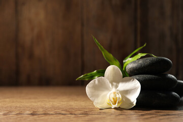 Obraz na płótnie Canvas Spa stones, beautiful orchid flower and bamboo sprout on wooden table, space for text