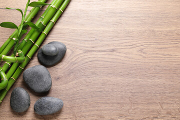 Spa stones and bamboo stems on wooden table, flat lay. Space for text