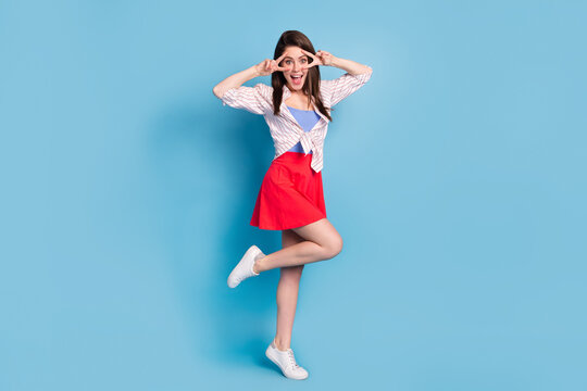 Full Size Portrait Of Charming Cheerful Lady Stand On One Foot Fingers Show V-sign Near Eyes Isolated On Blue Color Background