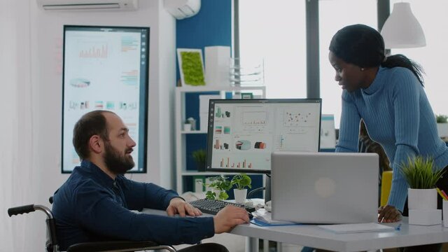 African entrepreneur making project presentation for invalid handicapped colleague sitting immobilized in wheelchair, planning strategy of company. Businesspeople working in startup financial office