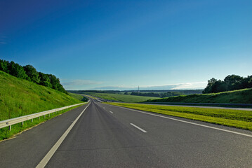 Obraz premium A long highway stretches into the distance under a blue sky and white clouds