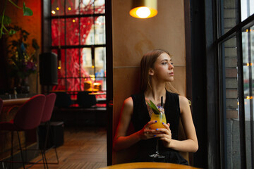 moody portraits of gorgeous blond girl with cocktail in fashion black outfit staying at the  bar in the club cafe or restaurant