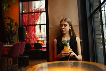 moody portraits of gorgeous blond girl with cocktail in fashion black outfit staying at the  bar in the club cafe or restaurant