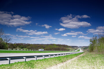 Fototapeta na wymiar A long highway stretches into the distance under a blue sky and white clouds