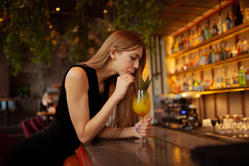 moody portraits of gorgeous blond girl with cocktail in fashion black outfit staying at the  bar in the club cafe or restaurant