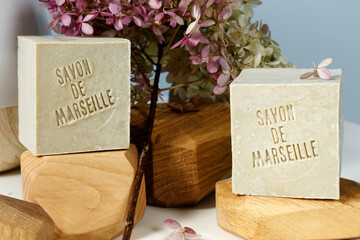 Natural soap with French language text (translate: Soap from Marseille) among pink flowers....