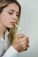 Portrait of a beautiful young blonde woman who lights a cigarette with the flame of the lighter