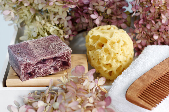Purple soap with loofah with bio bath accessories among pink flowers. Romantic bath arrangement.