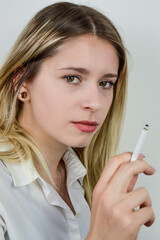 Portrait of a beautiful young blonde woman who is smoking a cigarette and is looking at camera