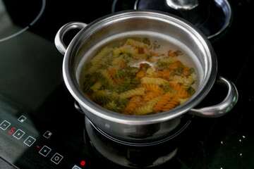 Pasta in a stainless steel pot of boiling water on a electric stove at home in the kitchen. Home cooking or italian cooking concept. A food theme: cooking multicolored organic pasta in hot water. 