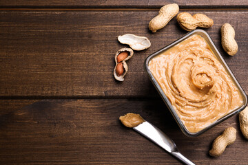 Yummy peanut butter in glass bowl on wooden table, flat lay. Space for text