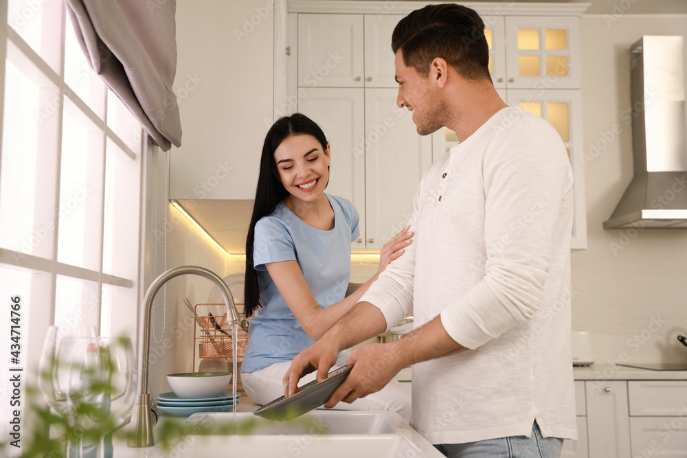 Wall mural Happy lovely couple washing dishes in kitchen