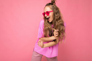 Attractive funny positive joyful young blonde woman wearing everyday stylish clothes and modern sunglasses isolated on colorful background wall looking to the side