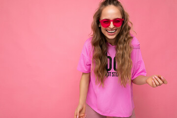Photo shot of beautiful happy smiling young dark blonde woman wearing casual clothes and stylish sunglasses isolated over colorful background looking at camera