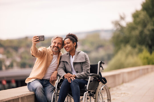 Adult couple, woman in a wheelchair, taking photos with her man.