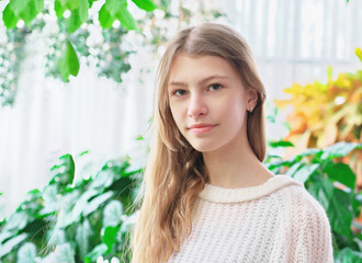 portrait of a teenager girl in her house in house garden room. green plants on a background. calm confident teen looking at camera