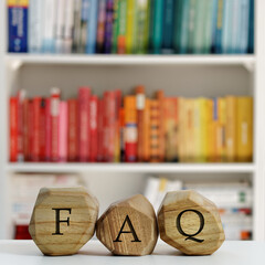 Letters FAQ written on wooden irregular blocks in front of blurred bookshelf. Frequently asked questions concept.