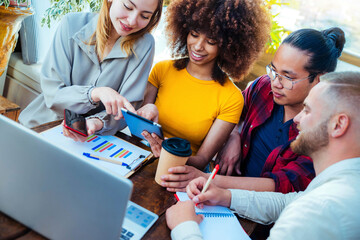 Multiracial diverse coworkers using tablet device on creative office - College students with laptop while sitting at table - Group study for school assignment