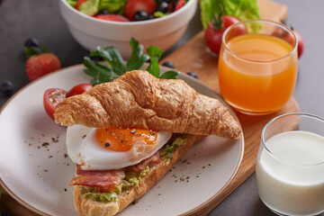Delicious breakfast with fresh croissants, bacon sandwich with fried egg. milk served, orange juice. strawberry, butterhead, blackberry salad. full american healthy breakfast top view.