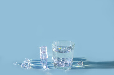 Glass of water with ice cubes on blue background, copy space