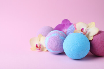 Colorful bath bombs and beautiful orchid flowers on pink background, space for text