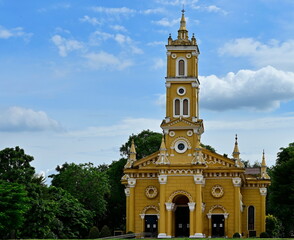 St Joseph Old Yellow Catholic Church (Beautiful Art and Architecture) In Ayutthaya, Thailand. There are bright green trees around the church and blue sky above the Chao Phraya River in front.
