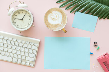 pink office desk table with blank paper mockup, alarm clock, coffee, .leaf, post-it. Top view with...