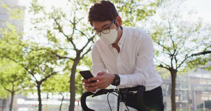 Asian man wearing face mask using smartphone while leaning on his bicycle on the street