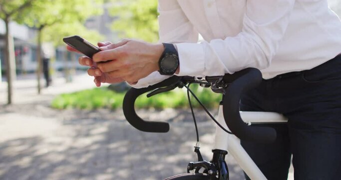 Mid section of man using smartphone while leaning on his bicycle on the street