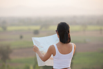 Adventurous girl navigating in with a topographic map in the beautiful mountains. woman while hiking and poles standing on a rocky mountain ridge and peaks in a healthy outdoors lifestyle concept.