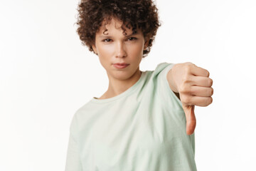 Young curly brunette woman showing thumb down at camera